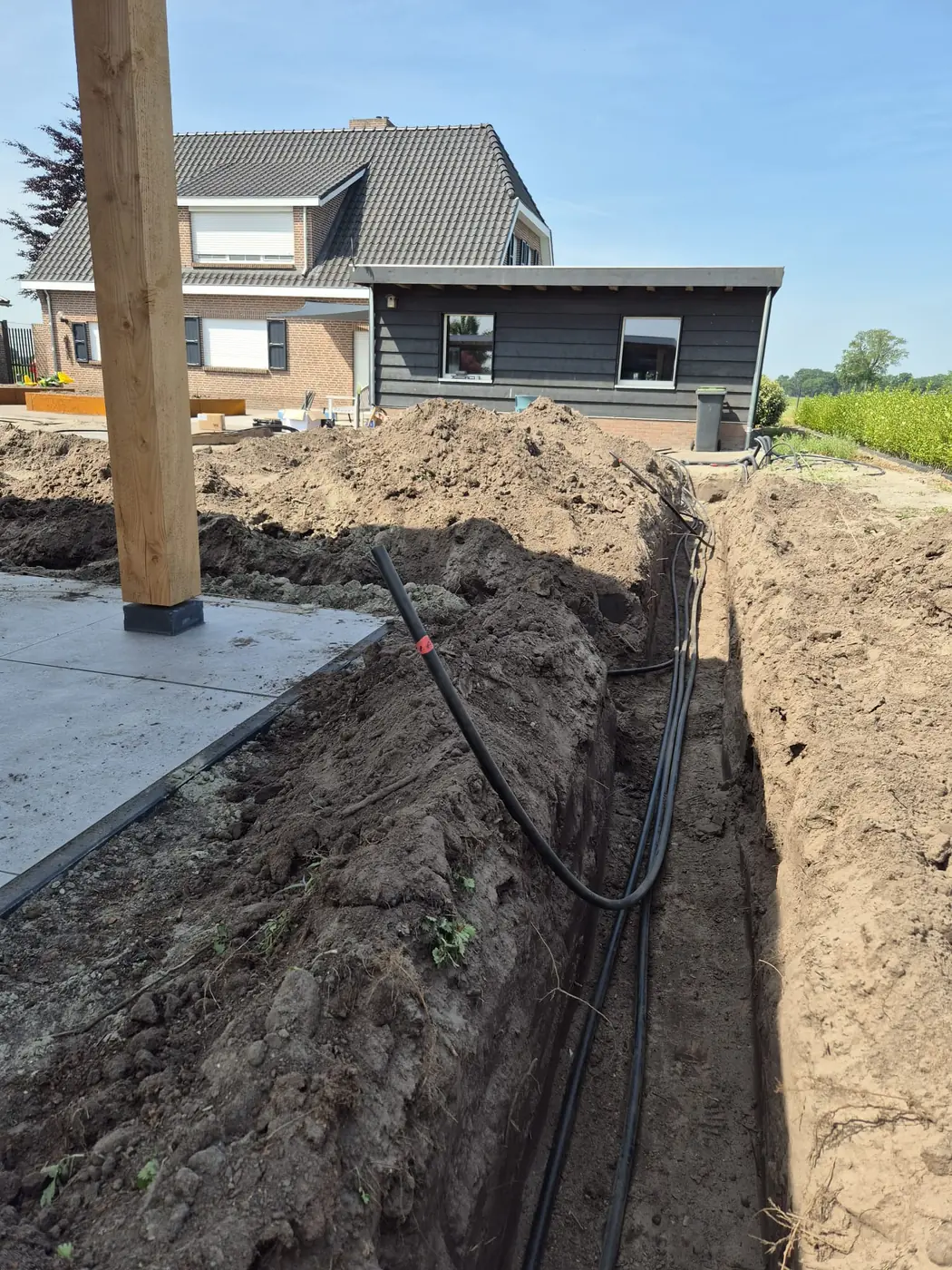 Aanleg van beregeningsleidingen in een sleuf naast een woning in aanbouw