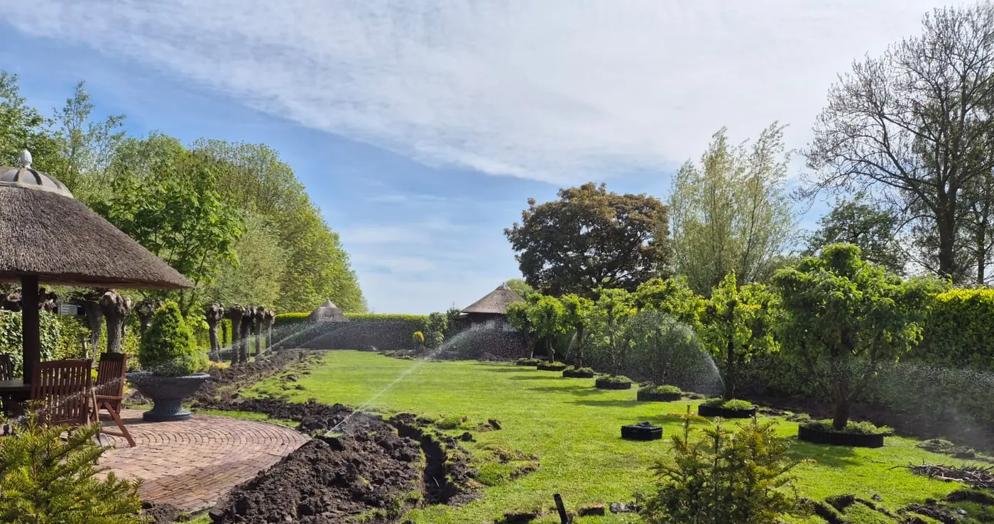 Sproeiers in werking in een tuin bij een rieten schuur